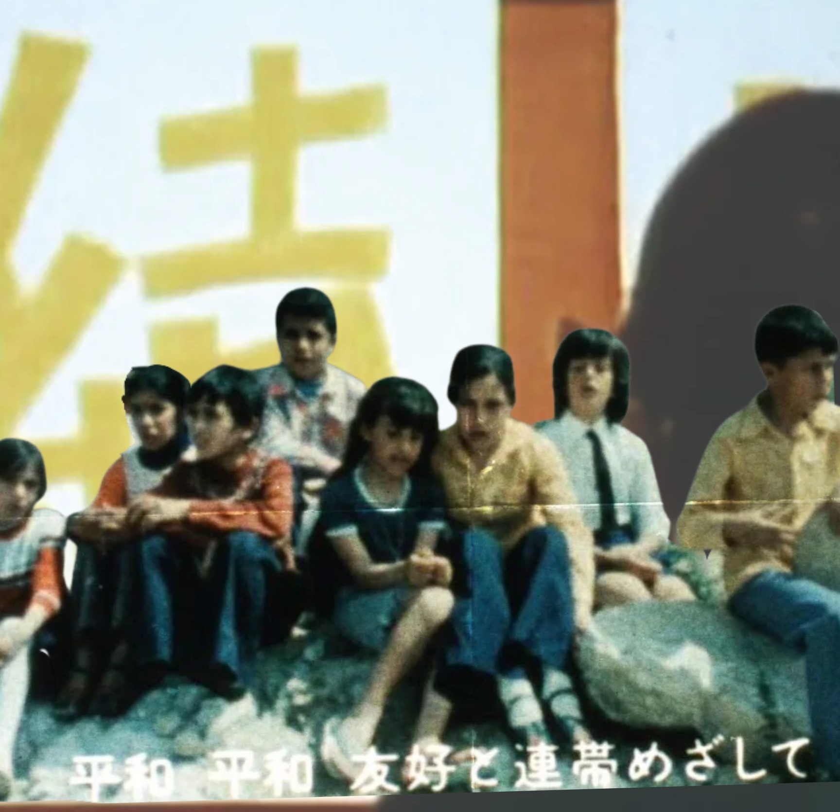 Children seated before a projection with Japanese lettering about peace, friendship and solidarity.